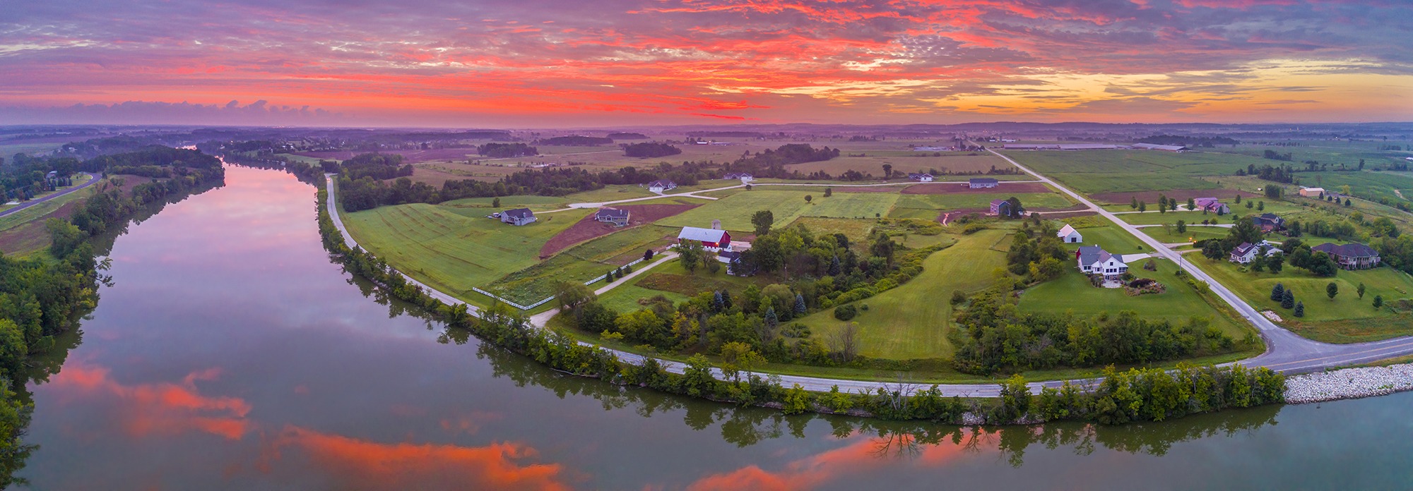 Red sky reflected in tranquil river at dawn, panoramic aerial view.